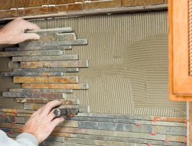 Photo of someone installing a tile backsplash by BanksPhotos/istockphoto.com